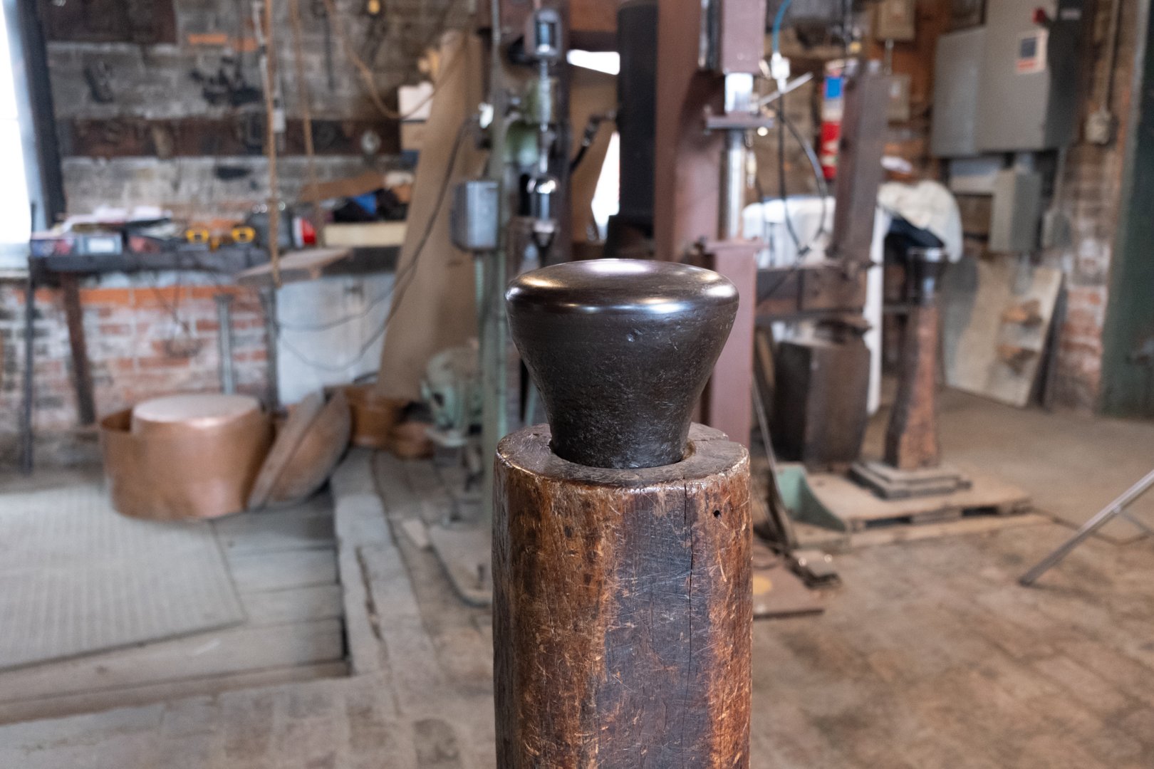 A black metal object with a rounded top, mounted on a wooden post in a woodworking shop.