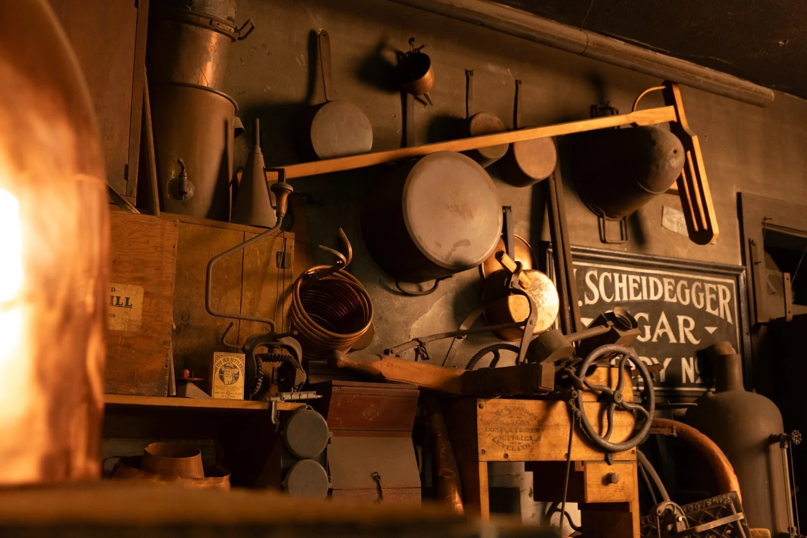 A wall filled with vintage tools, equipment, and signs, including pots, pans, and a framed sign that reads 'SCHEIDEGGER GEAR'.