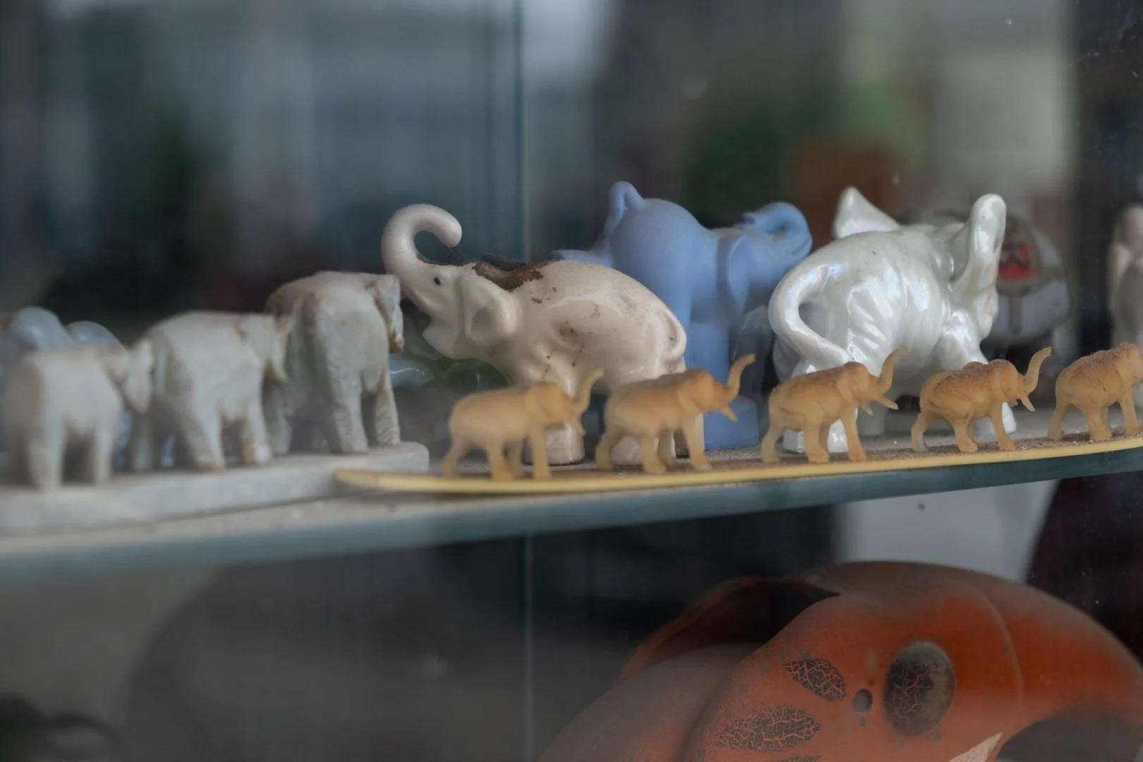 A collection of small ceramic and plastic elephant figurines and a row of tiny beige elephant toys displayed on a glass shelf.