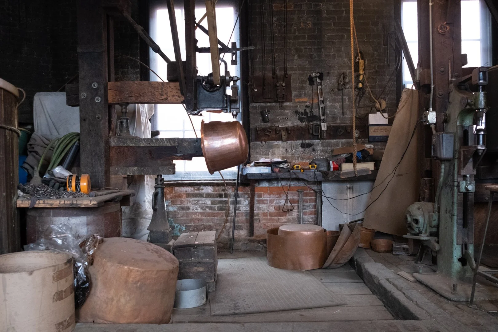 A woodworking or metalworking workshop with various tools, wood, and equipment, including a large machine, workbench, and storage areas.