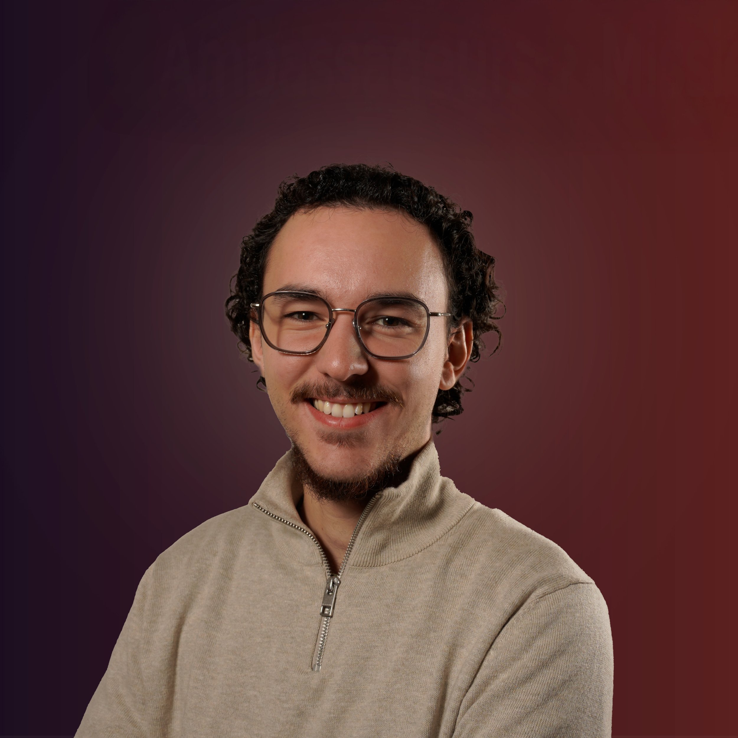 Portrait d'un homme souriant portant des lunettes et un pull beige, fond dégradé rouge et violet.