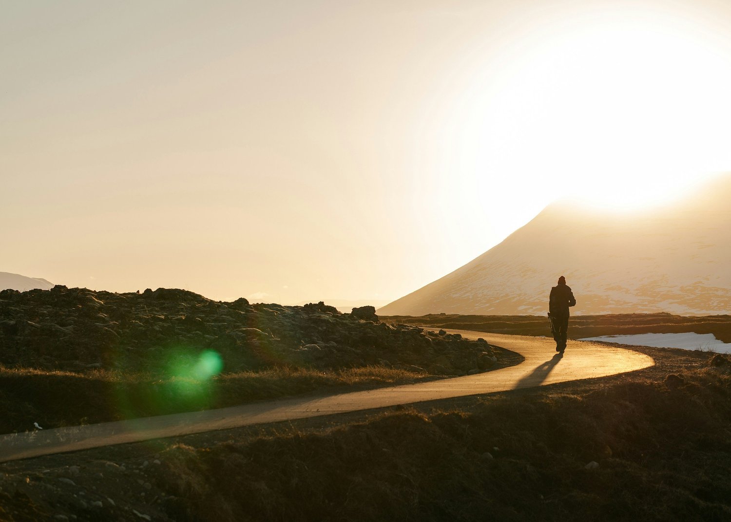 A person walking a winding path toward a low sun