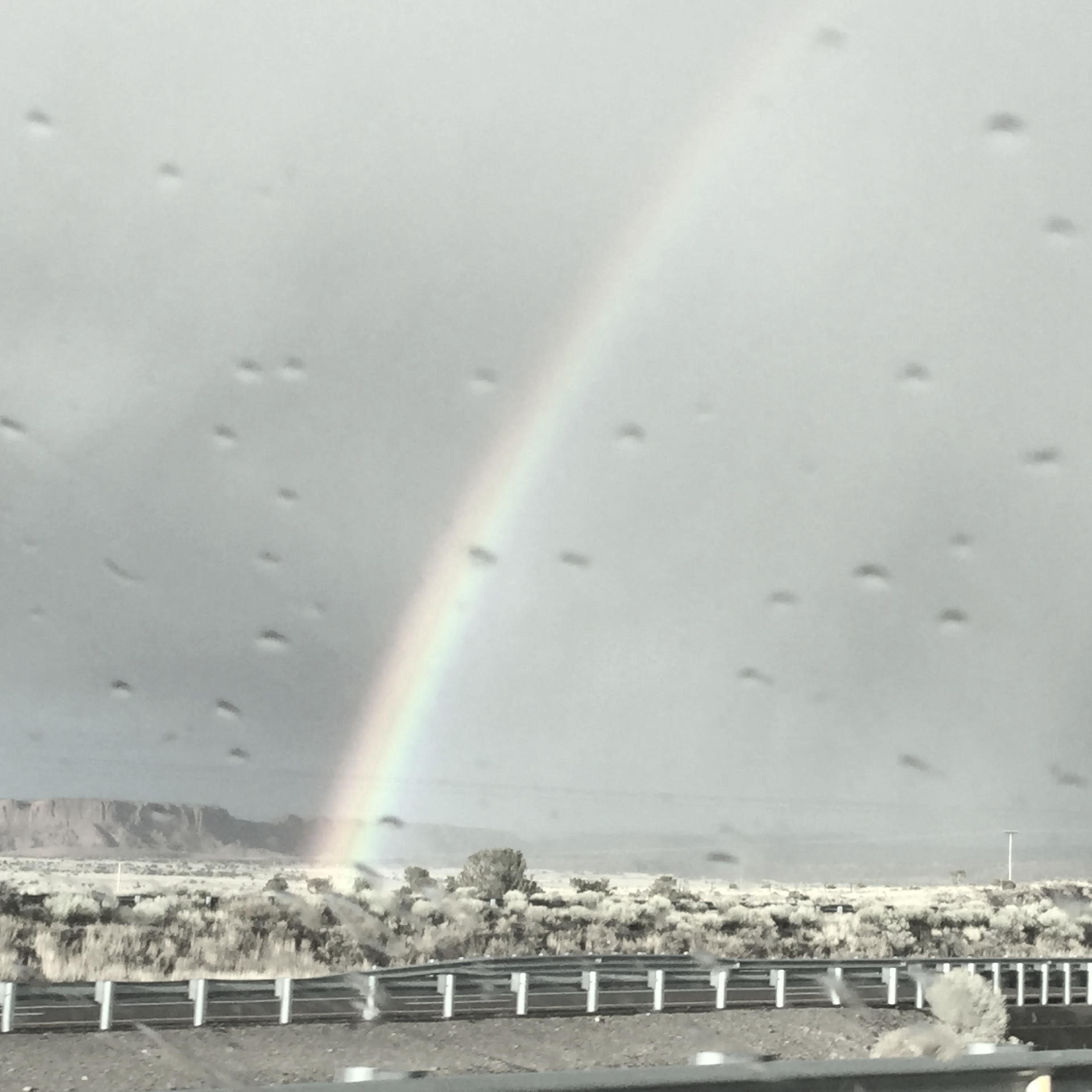 Rainbow over a desert landscape seen through a rain-spattered car window.