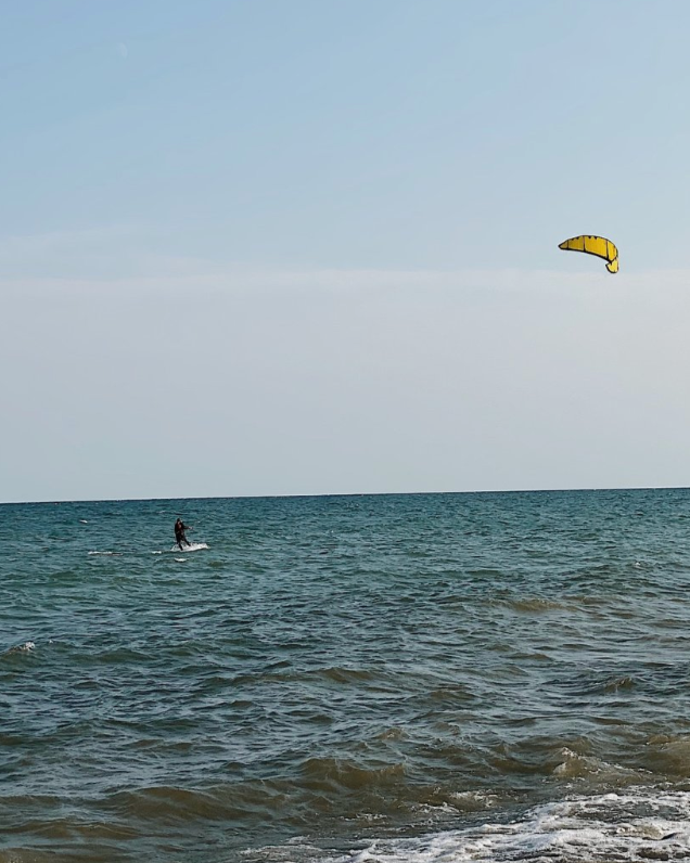 A person riding a jet ski on the ocean near the shore with a kite in the sky.