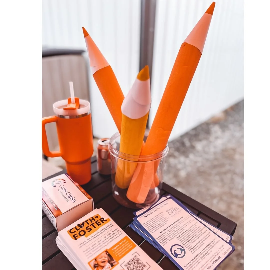 Colorful paper designs resembling large pencils or crayons in a glass jar, along with informational pamphlets on a table.