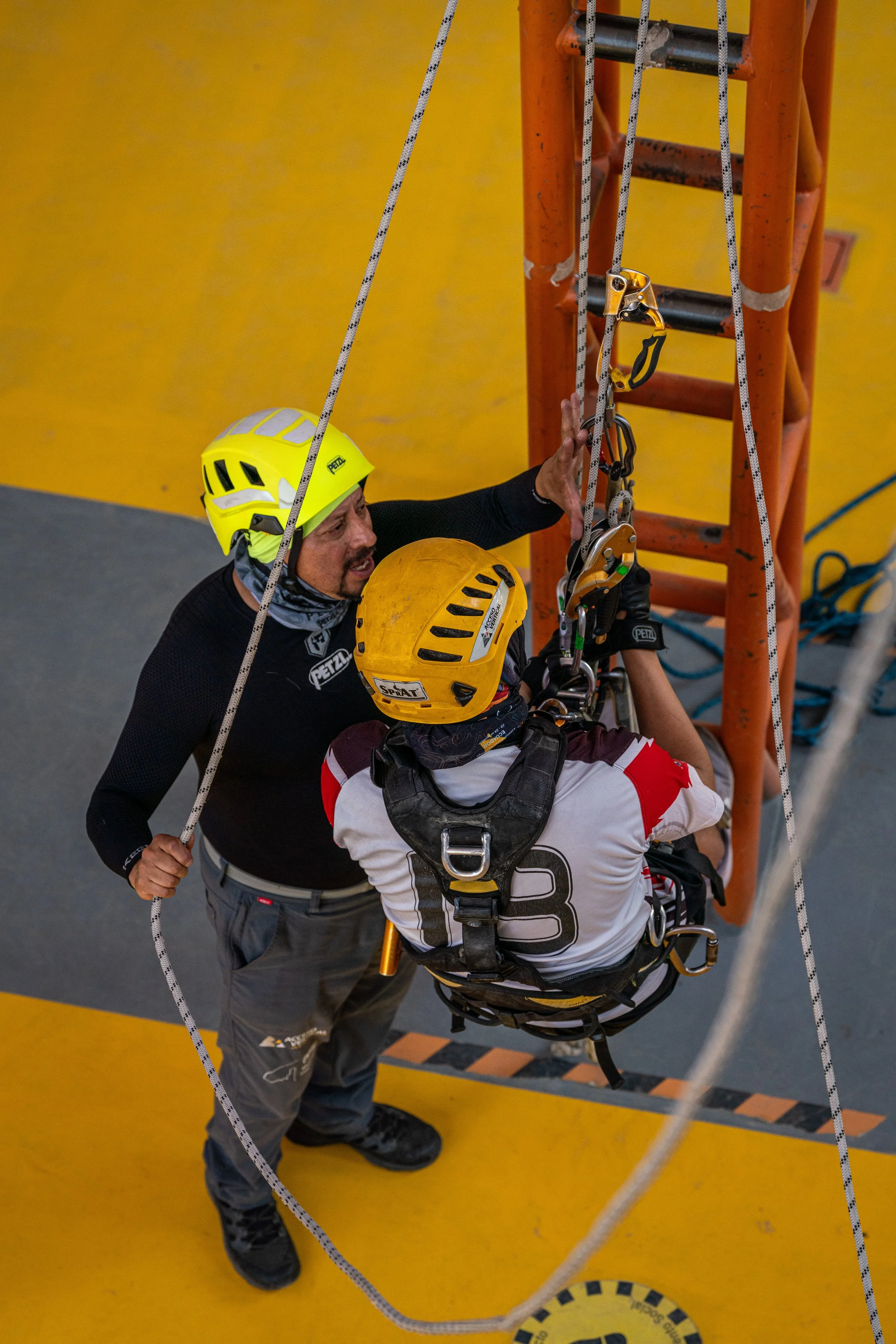 Una persona con cascos de escalada siendo asistida por otra en un entorno de escalada interior.