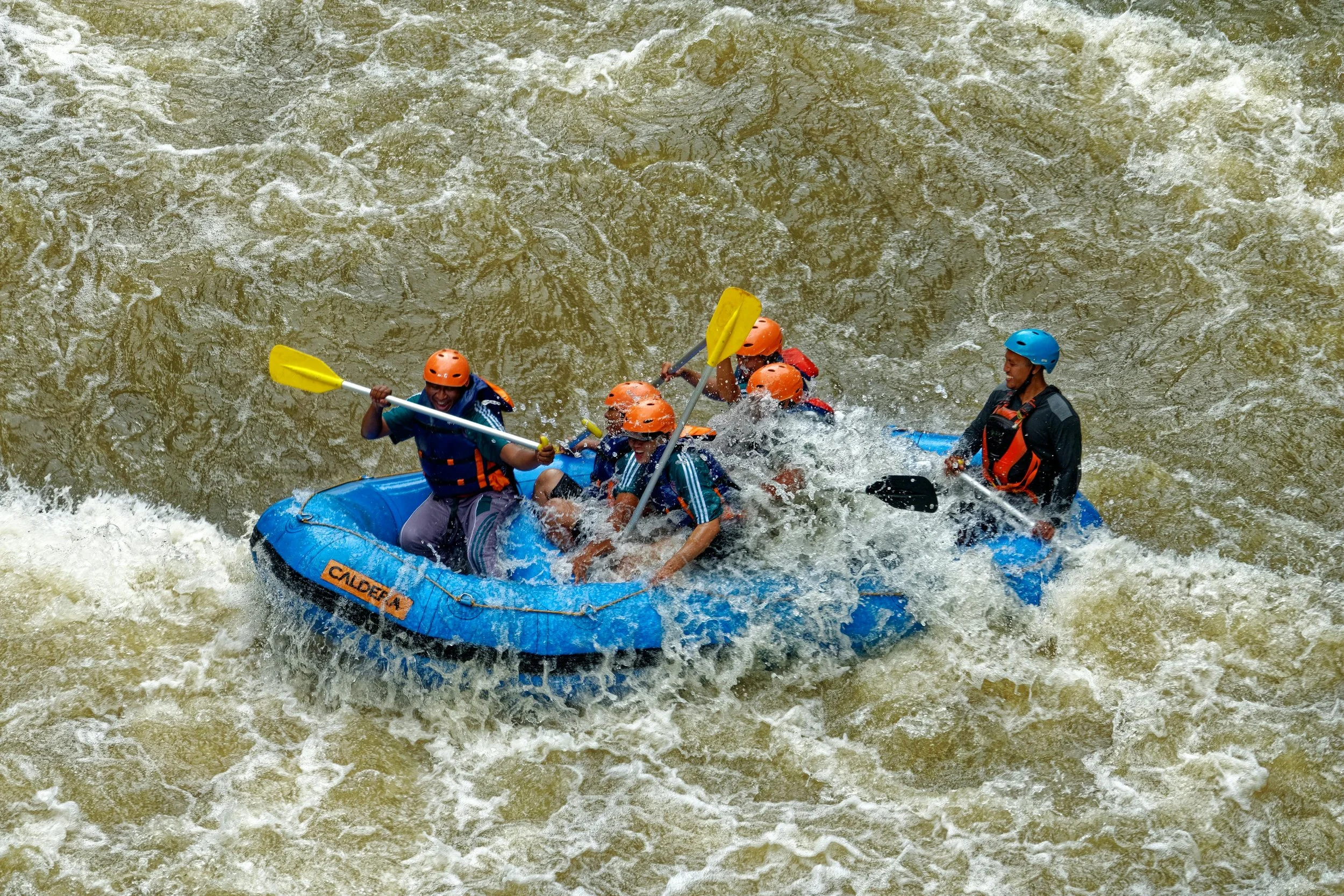 Grupo de personas practicando rafting en río turbulento, con cascos y chalecos salvavidas, utilizando remos