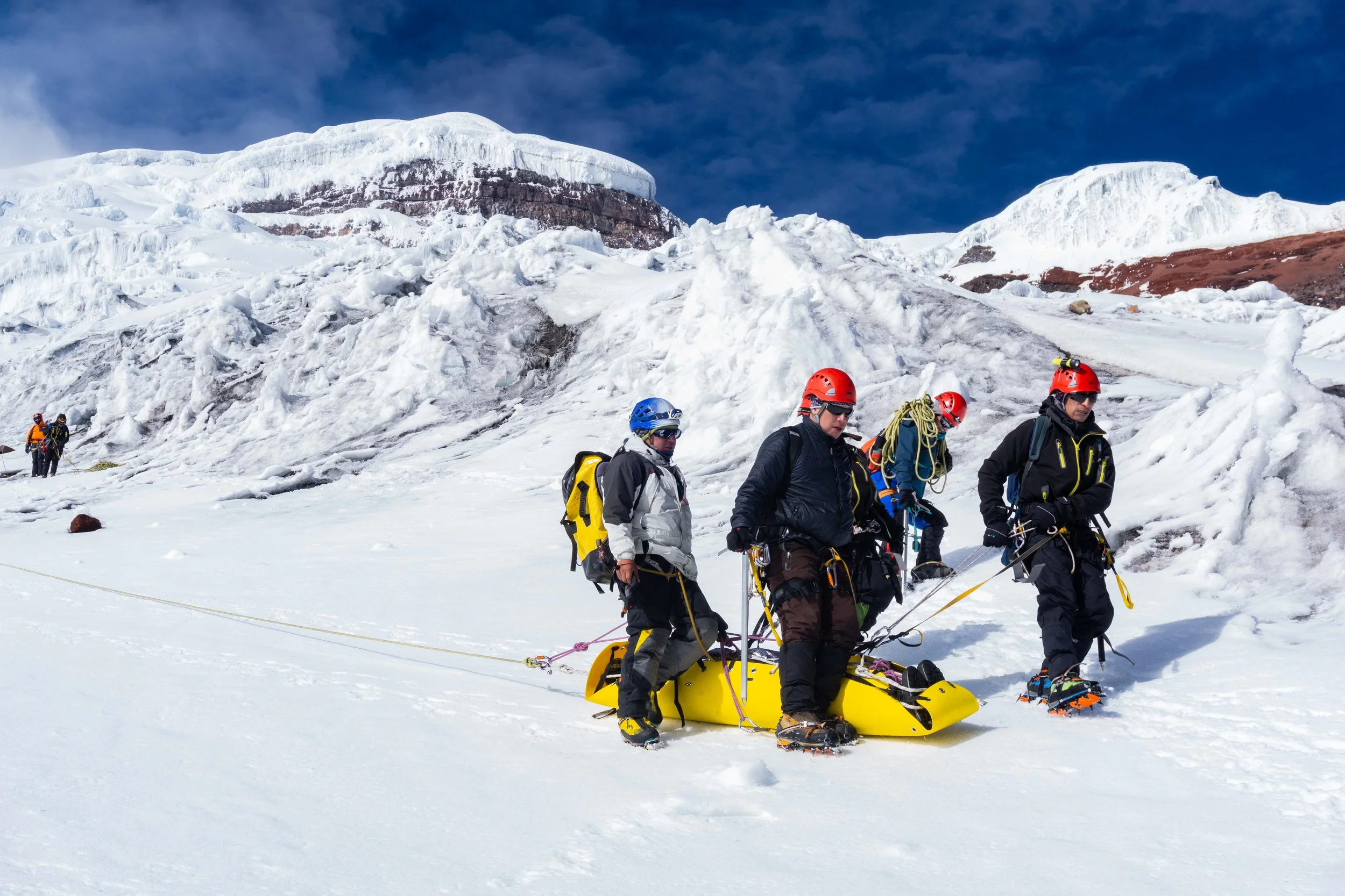 Un grupo de personas realizando rescate en la nieve en una zona de glaciares con montañas cubiertas de nieve al fondo.
