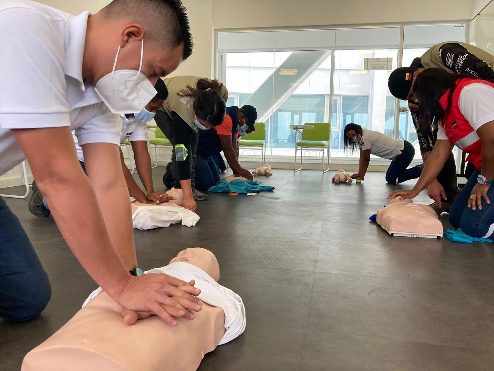 Grupo de personas practicando reanimación cardiopulmonar en mannequins en un aula, haciendo técnicas de primeros auxilios.