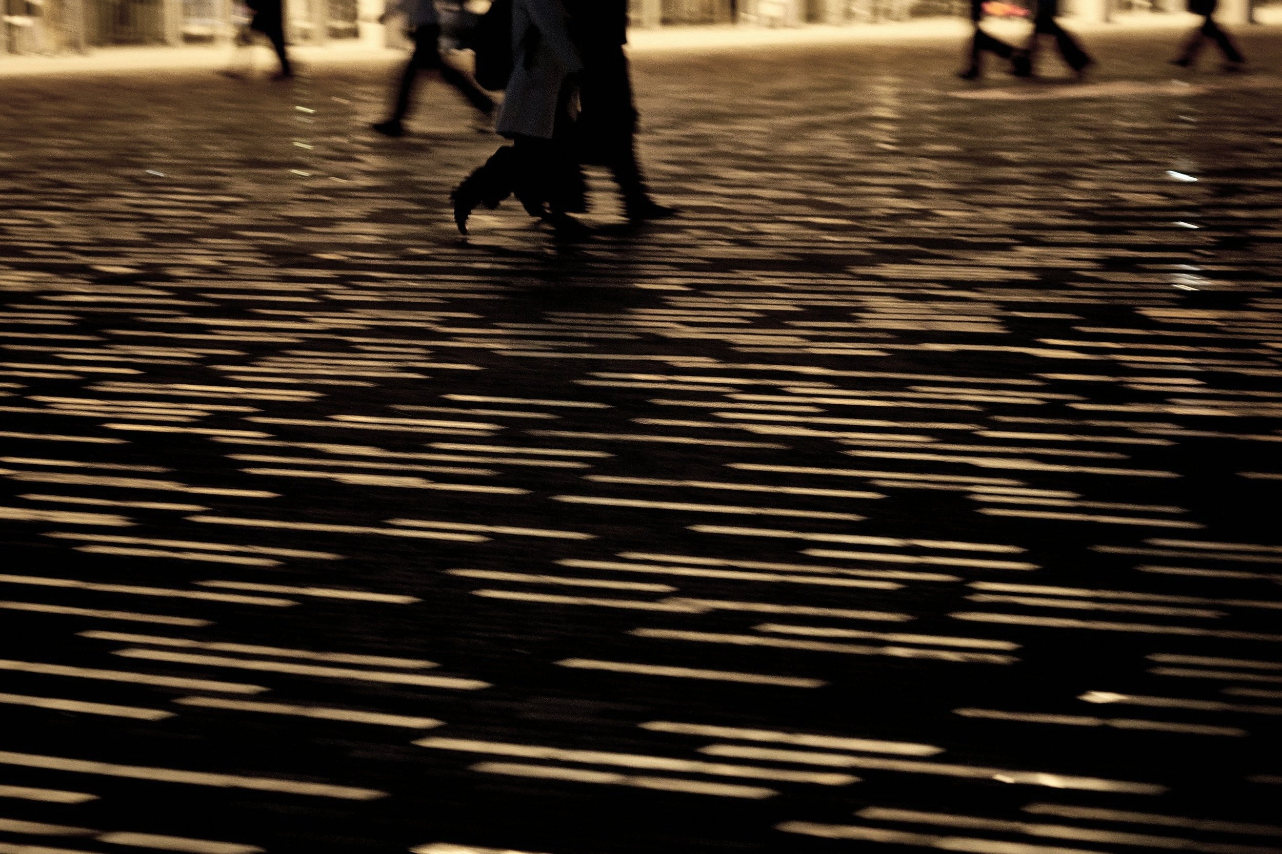 People walking on a cobblestone street at night, with the streetlights reflecting on the wet surface.