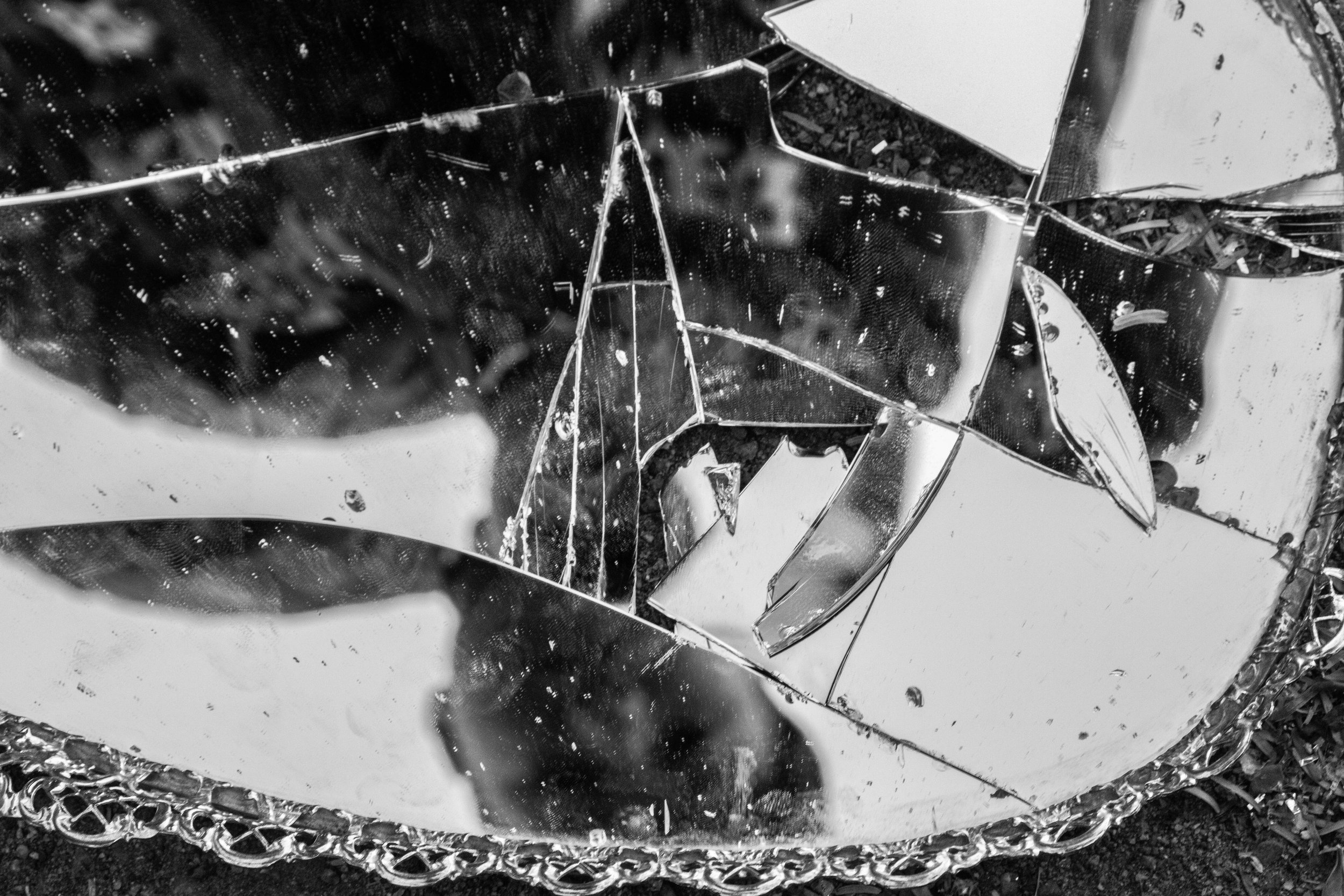 Broken and shattered mirror pieces reflecting light and surroundings, with some small debris, framed with a decorative border.