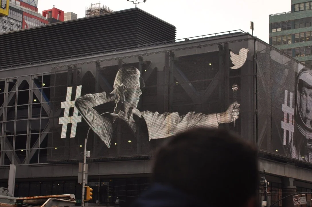 Large billboard featuring a black and white image of a man shooting an arrow whilst wearing suit and tie in New York.