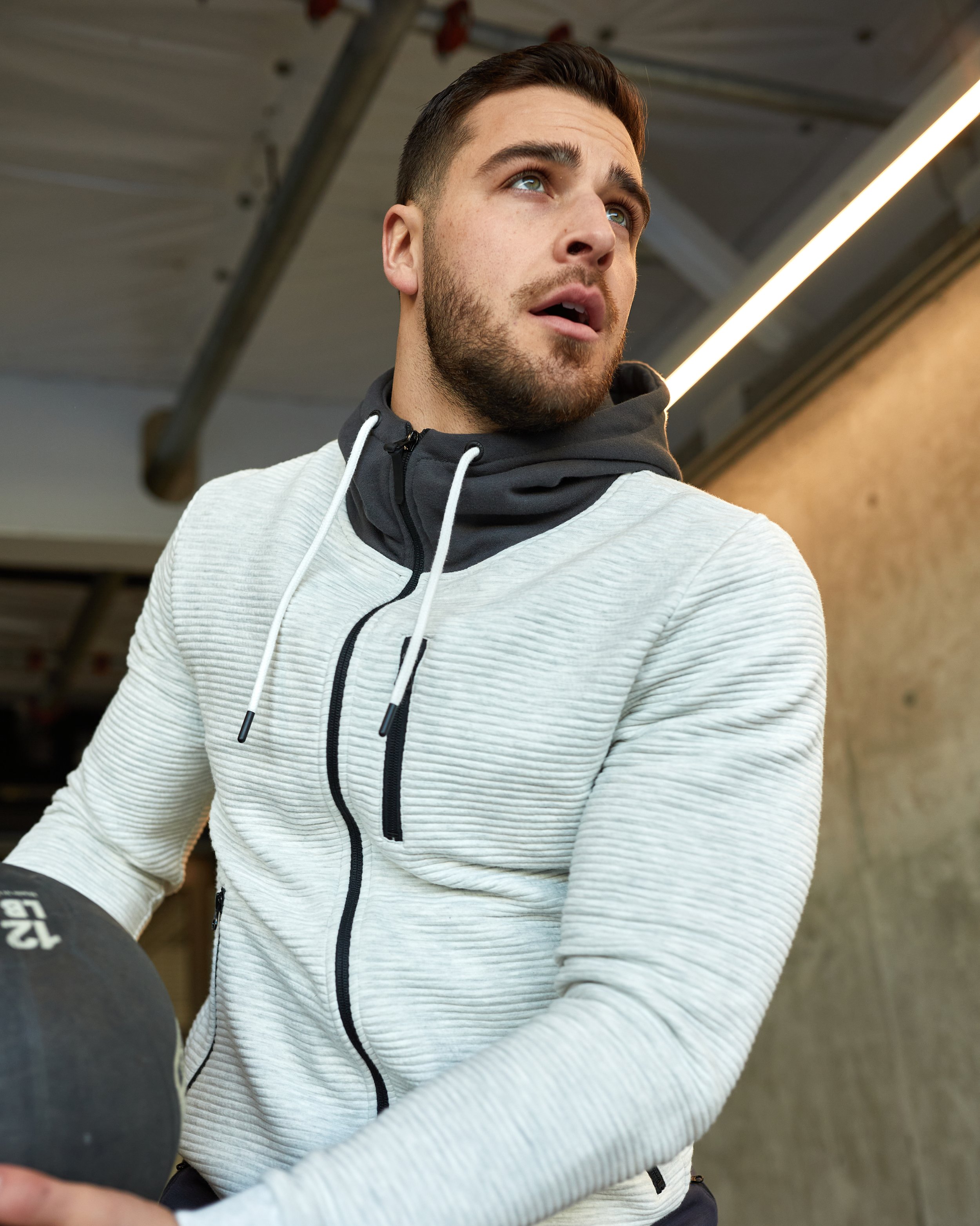 A young man in workout attire holding a medicine ball, looking upwards with a focused expression in a gym.