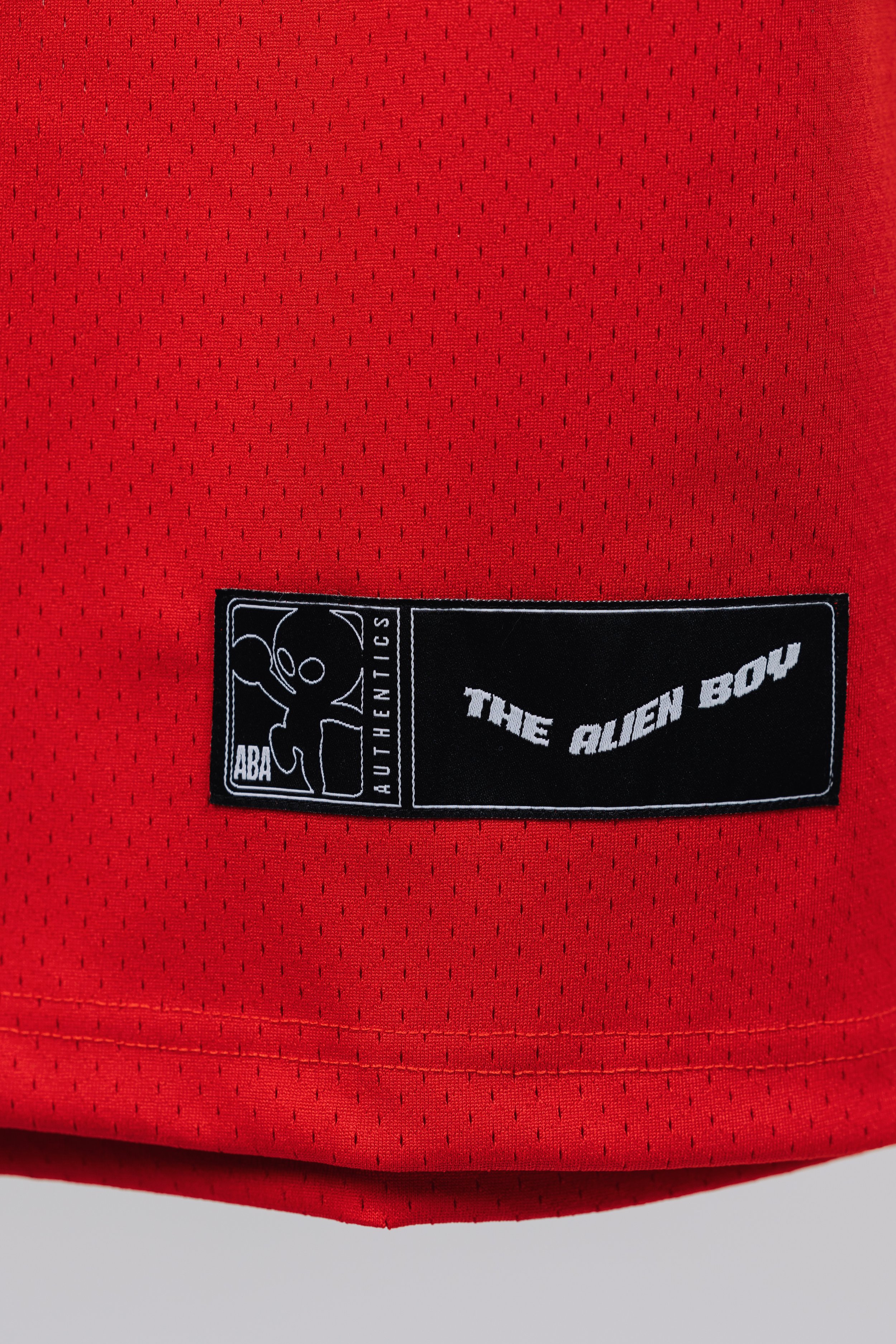 Close-up of a red fabric with a black label reading "The Alien Boy" and an illustration of an alien head, associated with ABA Authentic branding.