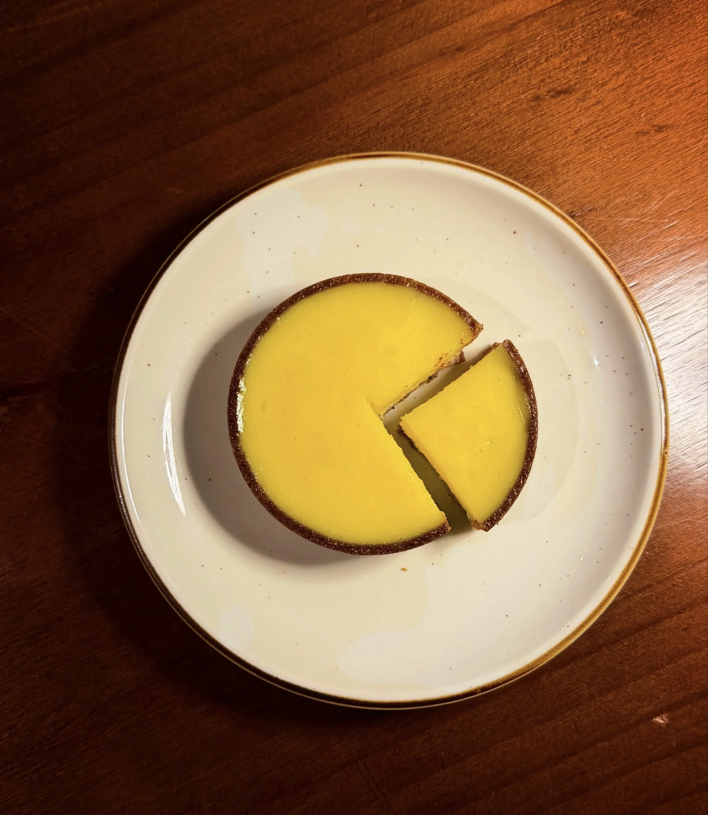 A yellow tart with a chocolate crust on a white plate, with one slice cut out.