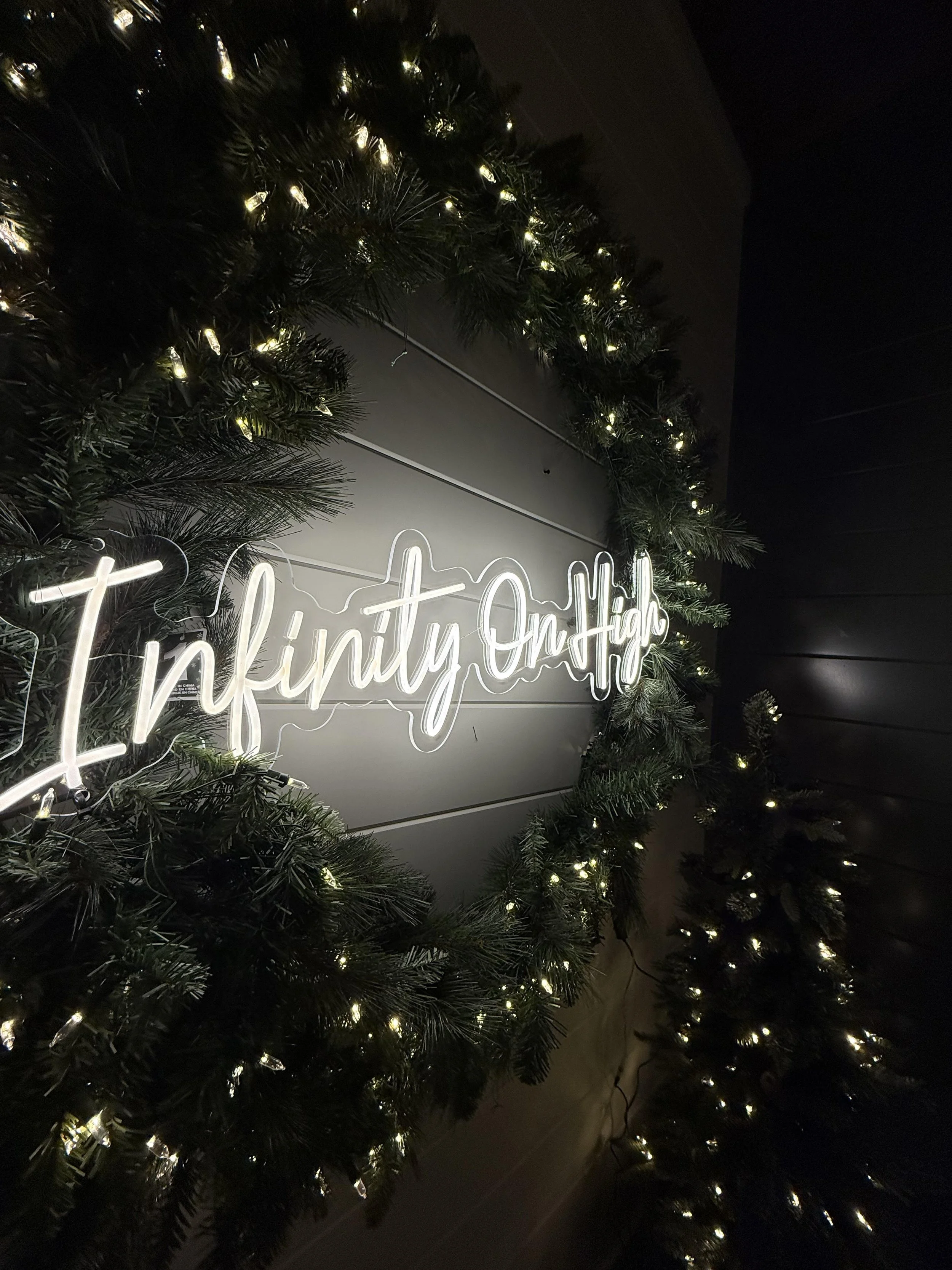 A neon sign that says 'Ininity On Hub' surrounded by green Christmas garland with white lights.