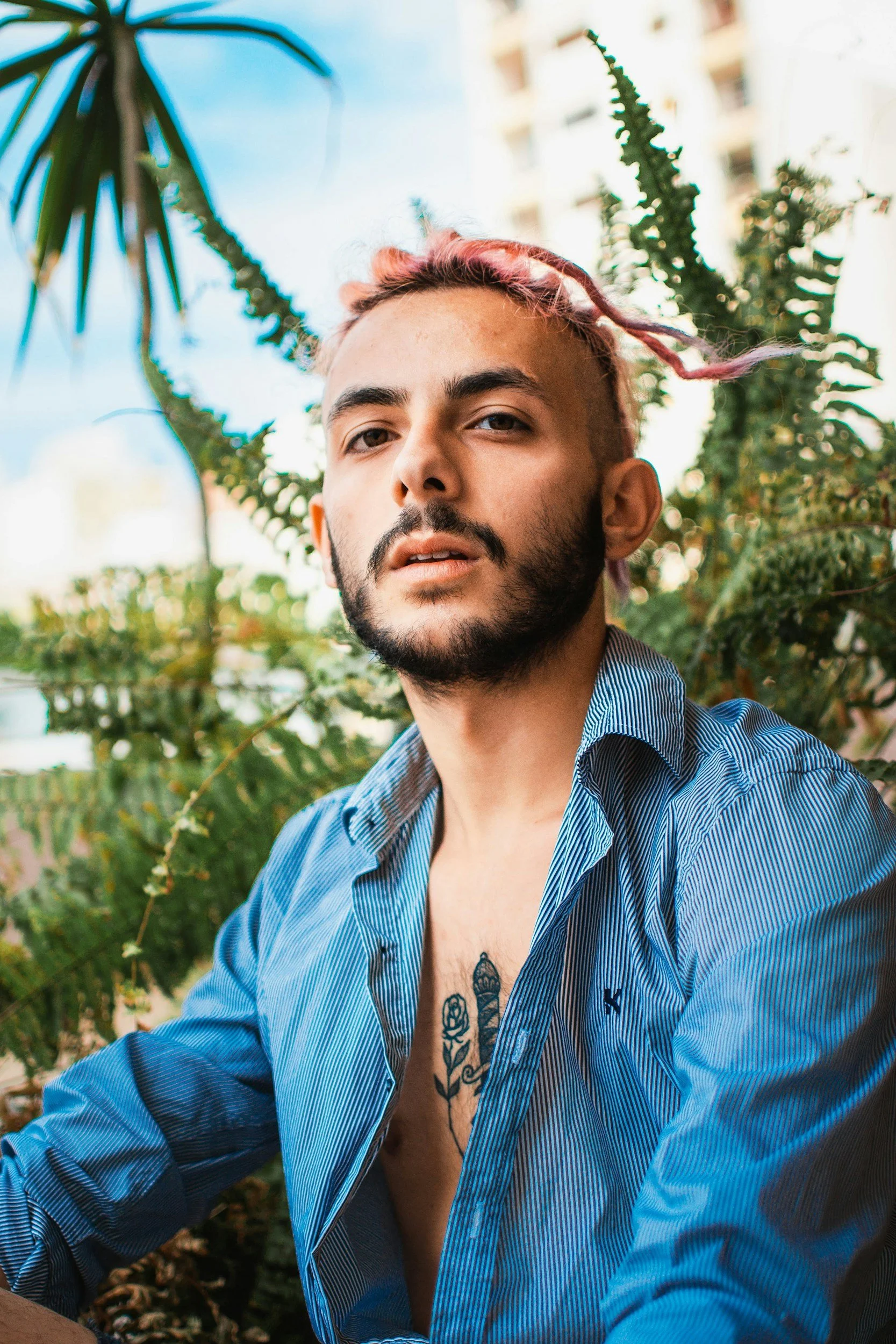 queer man with pink hair, blue shirt, and chest tattoo staring forward with curiosity in trauma therapy in Concord, NC