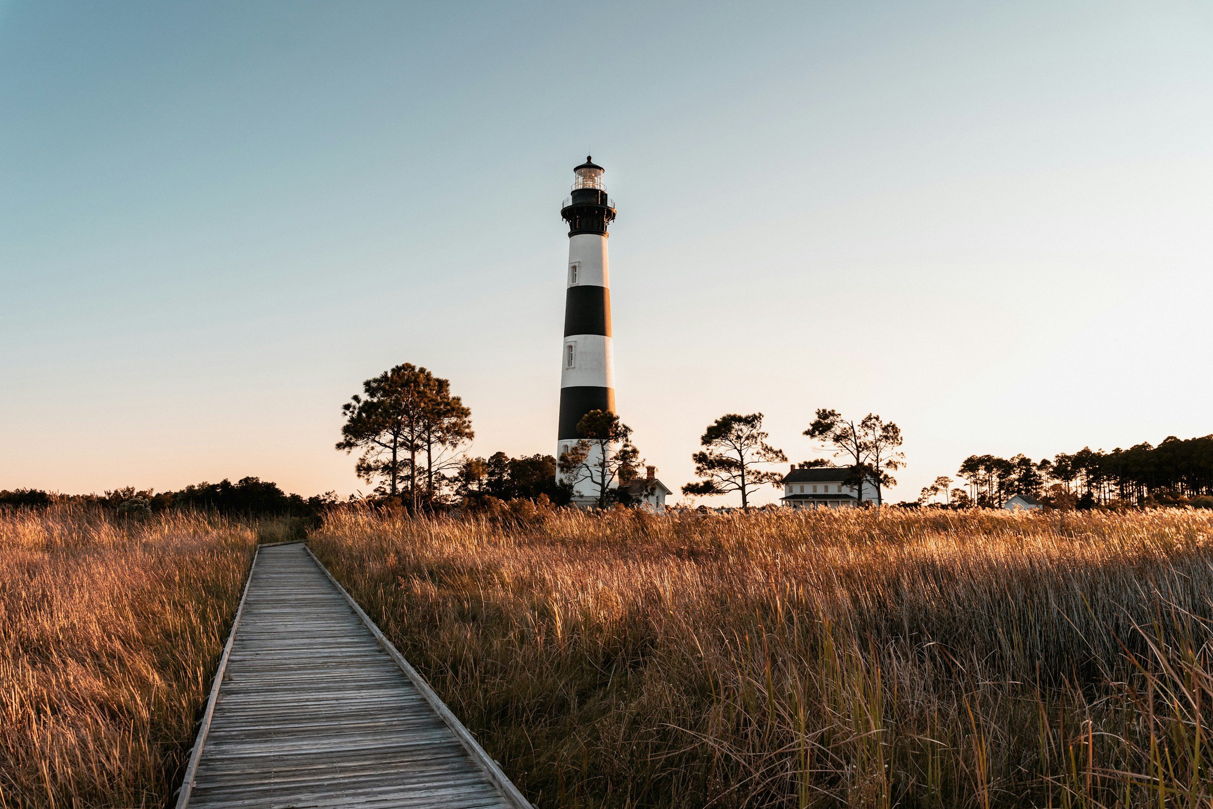 black and white striped lighthouse behind field of tall grass and wooden boardwalk in North Carolina