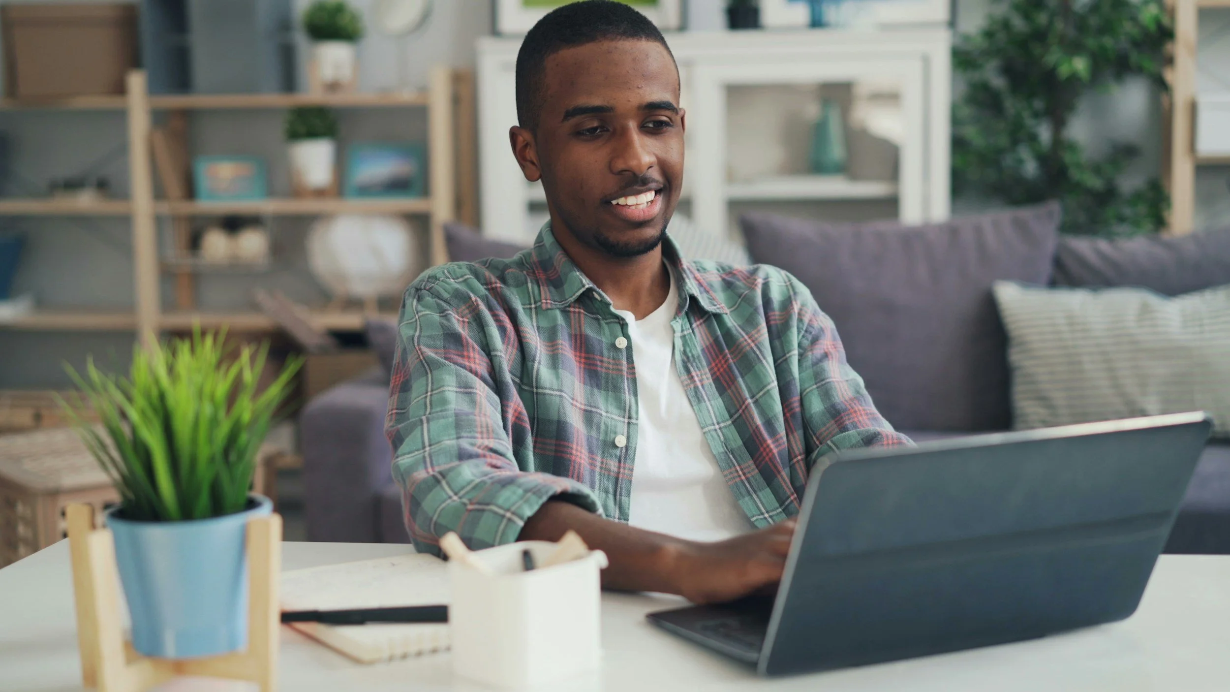 smiling young black man sitting at white desktop using tablet for online polyamory therapy