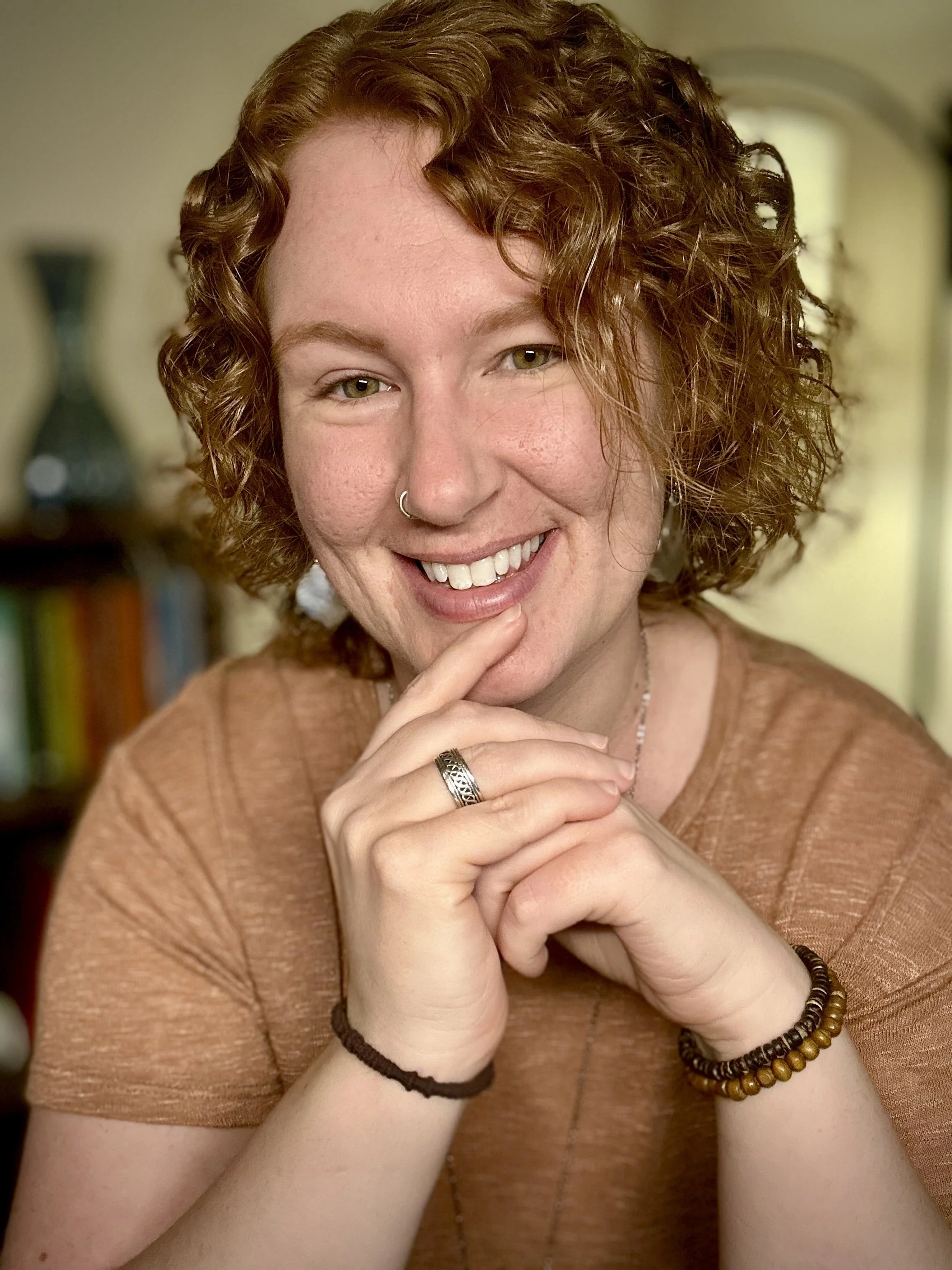 female trauma therapist with short surly red hair wearing orange shirt smiling with chin on folded hands