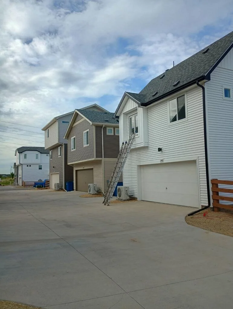 Multiple new two-story townhouses with garages and air conditioning units, under a partly cloudy sky, in a residential area.