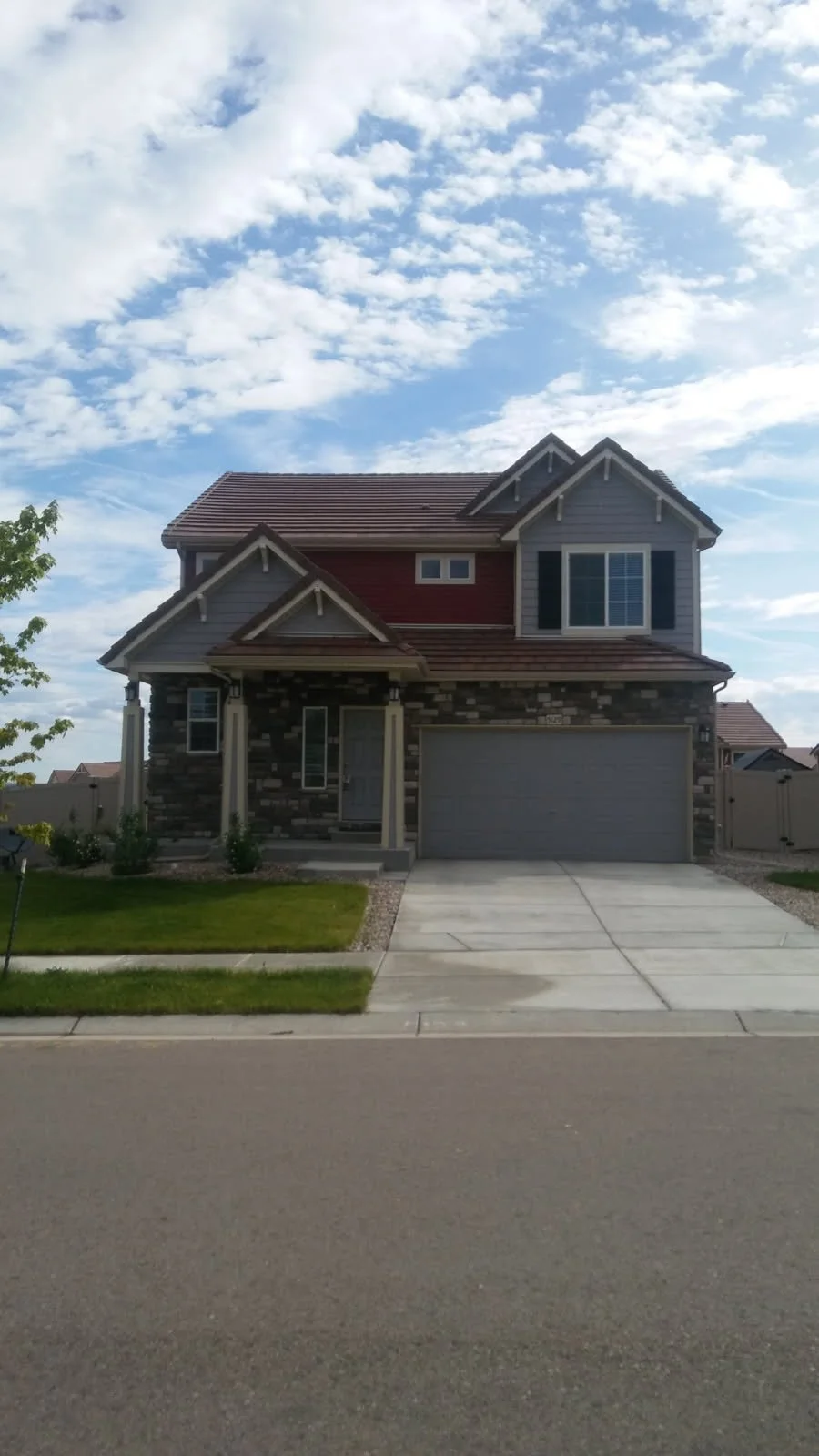 A two-story house with a brick and siding exterior, a gable roof, a two-car garage, and a small front porch, set against a partly cloudy sky.