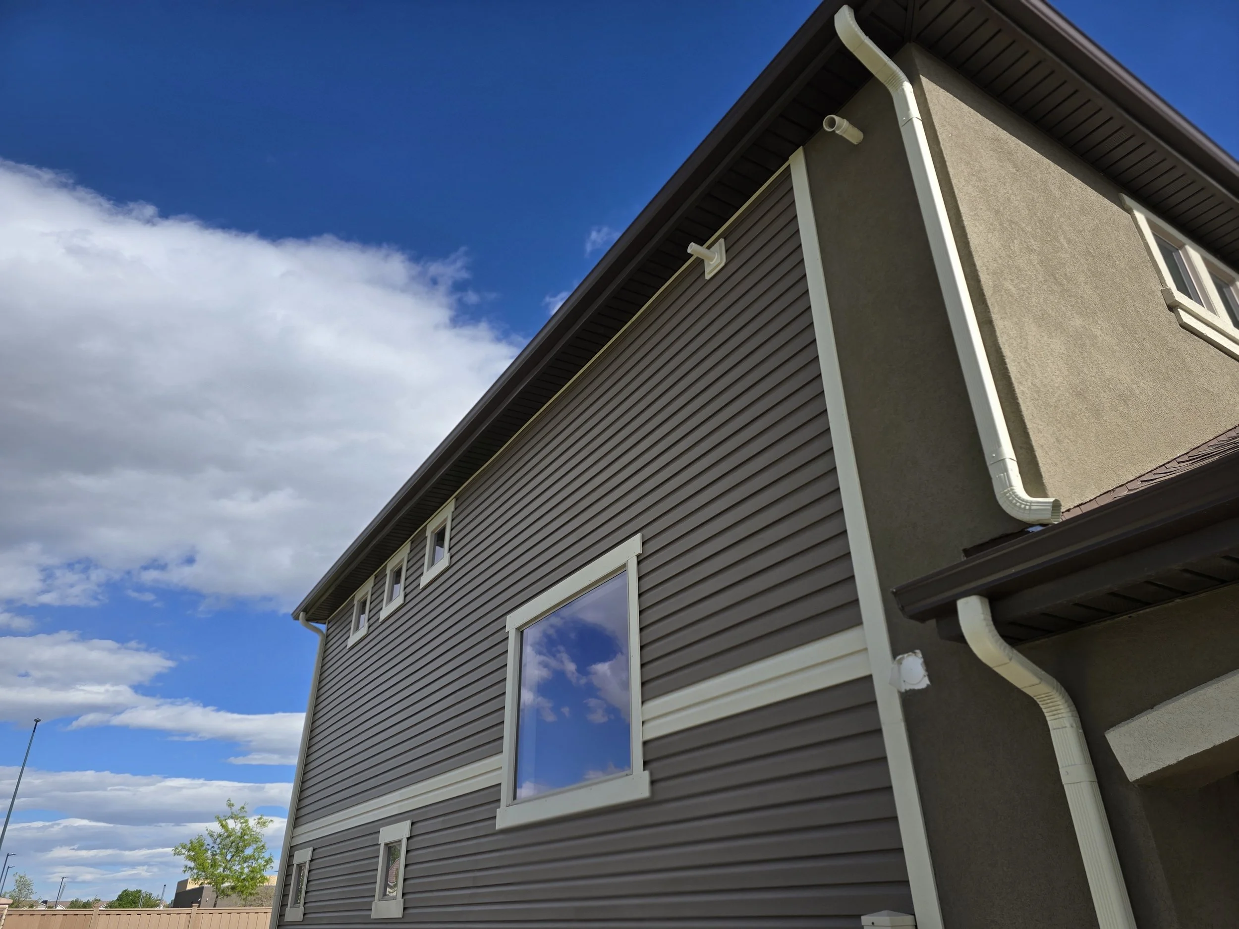 Close-up of a house exterior showing siding, window, gutters, and roof against a partly cloudy sky.