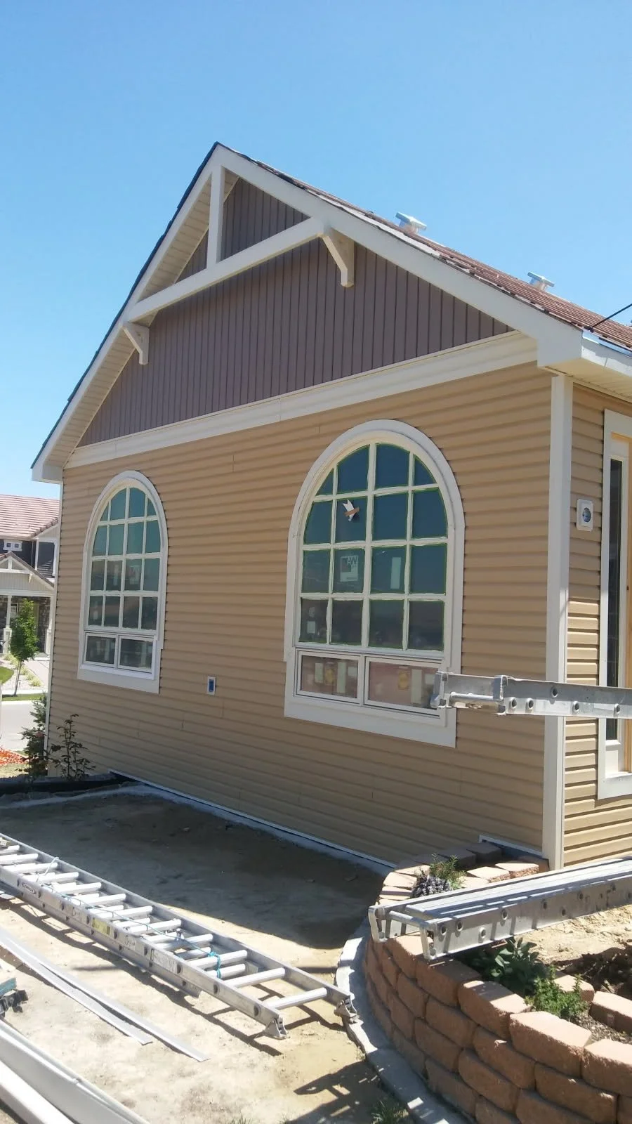 The exterior of a house under construction with beige vinyl siding, large arched windows, and a gabled roof.