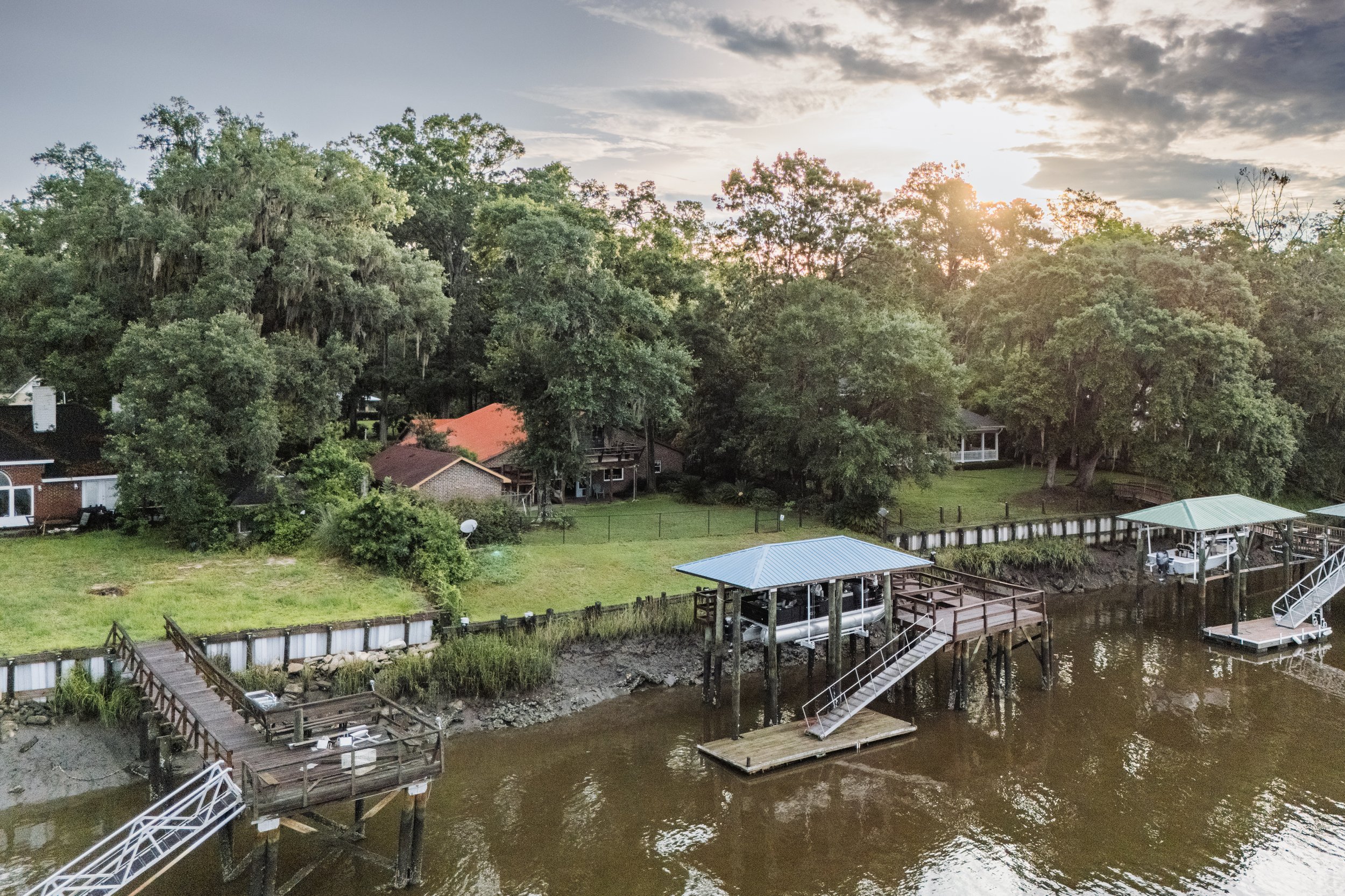 Sunset over a waterfront with trees, houses, and multiple boat docks with boat slips and stairs.