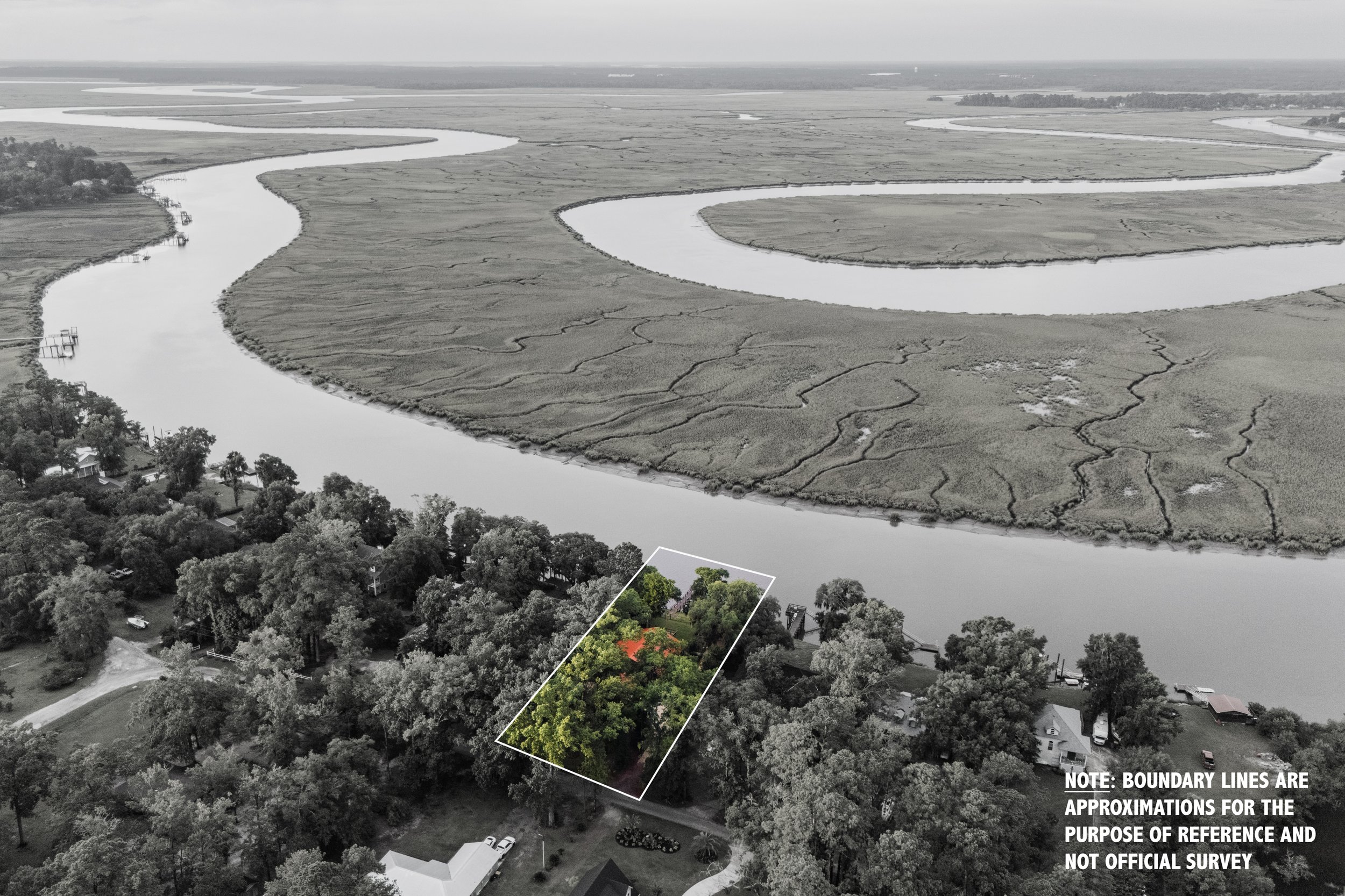 Aerial view of a property outlined in white near a winding river, surrounded by trees, with a marshland landscape in the distance. The image is mostly in black and white, with the property highlighted in green and red.