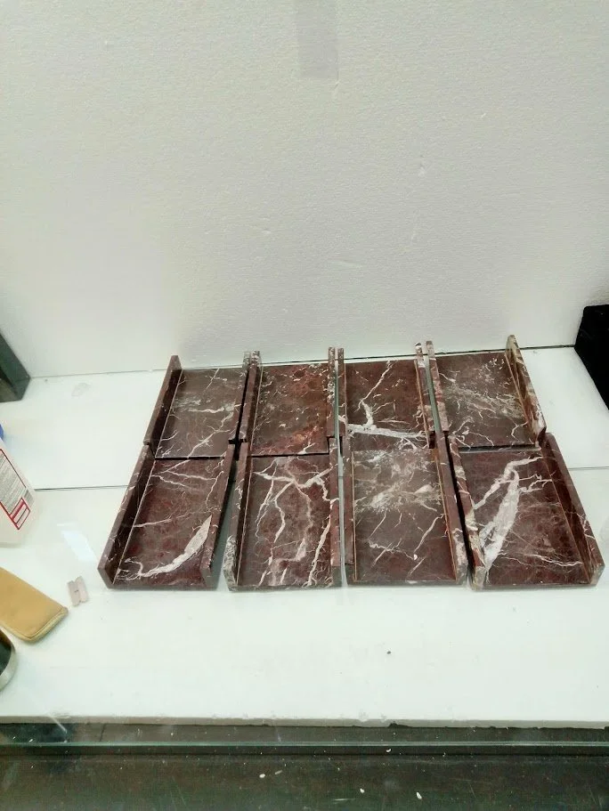 Multiple empty marble trays or boxes arranged on a white shelf or table, with small objects and a spray bottle nearby.