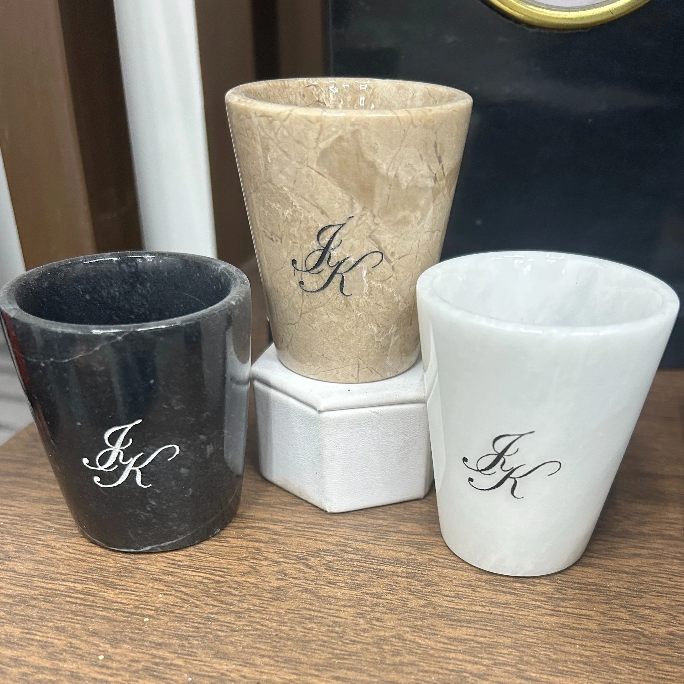 Three marble-effect candle holders with the initials J K, in black, beige, and white, on a wooden surface.