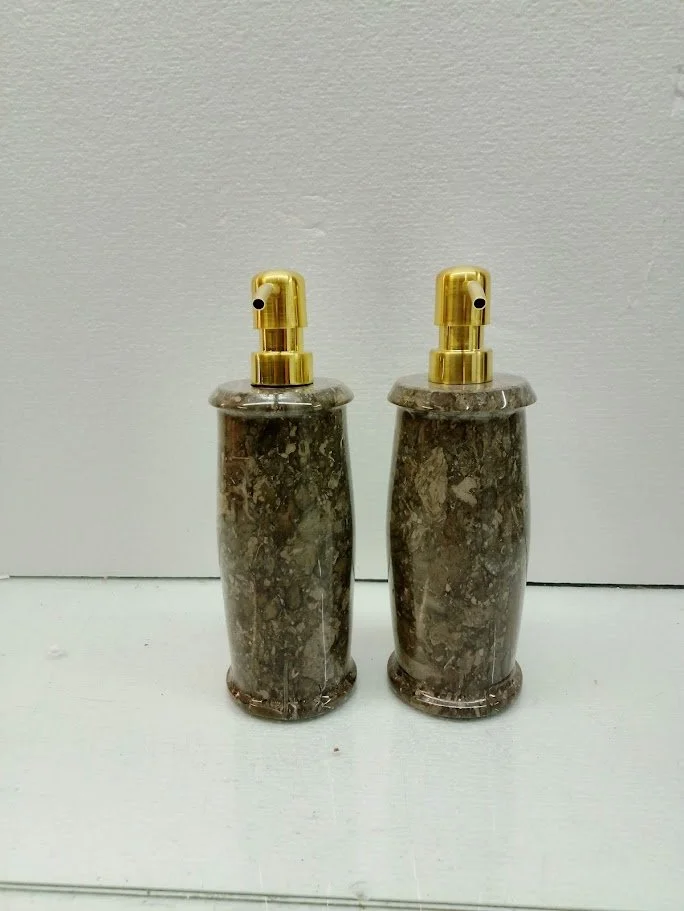 Two soap dispensers with marble bodies and gold pumps on a white surface against a white wall.