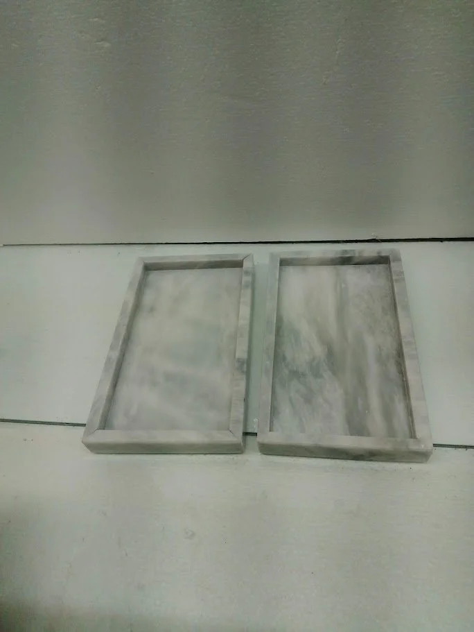 Two rectangular marble trays on a concrete floor against a metal wall.