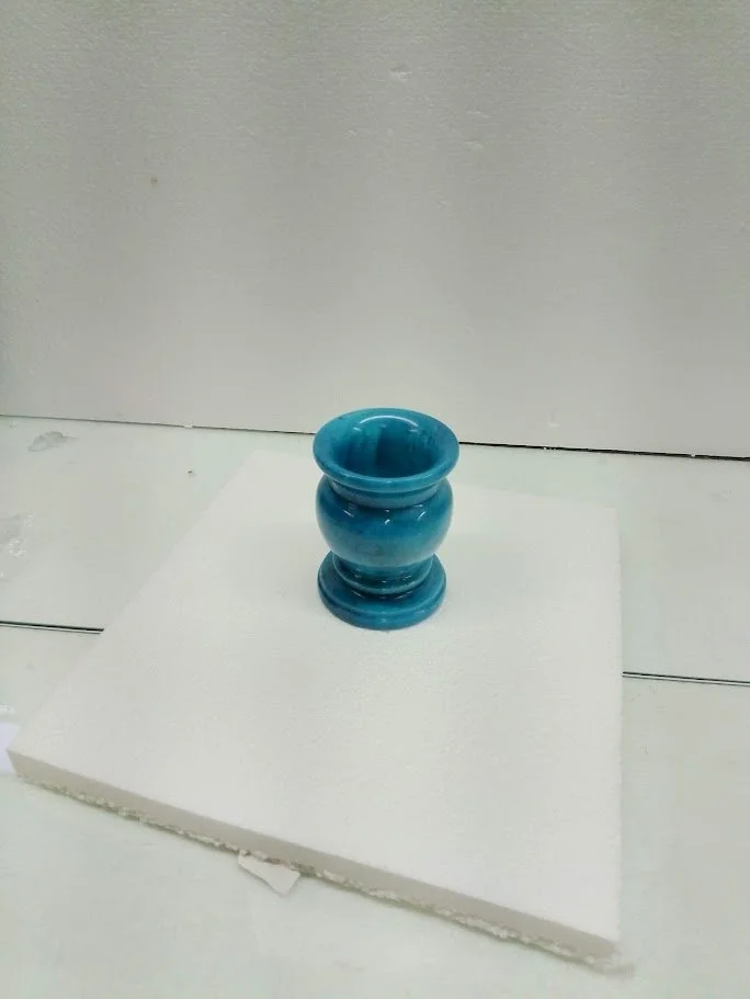 Blue glazed ceramic vase on a white display platform in an art display setting.