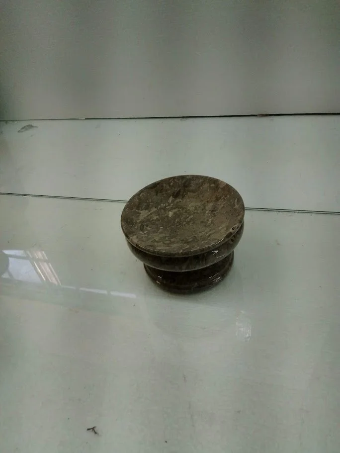 A small, round, marble-like stool or decorative object on a shiny floor, against a white wall.