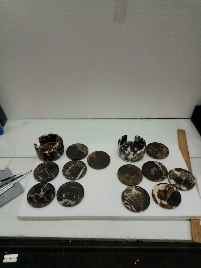 Polished black marble slabs and rounds arranged on a white surface, with tools and a ruler visible at the edges.