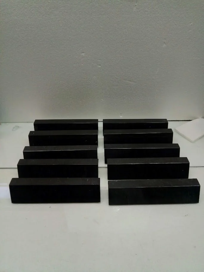 Ten black rectangular objects arranged in two rows on a white surface, with a gray wall in the background.