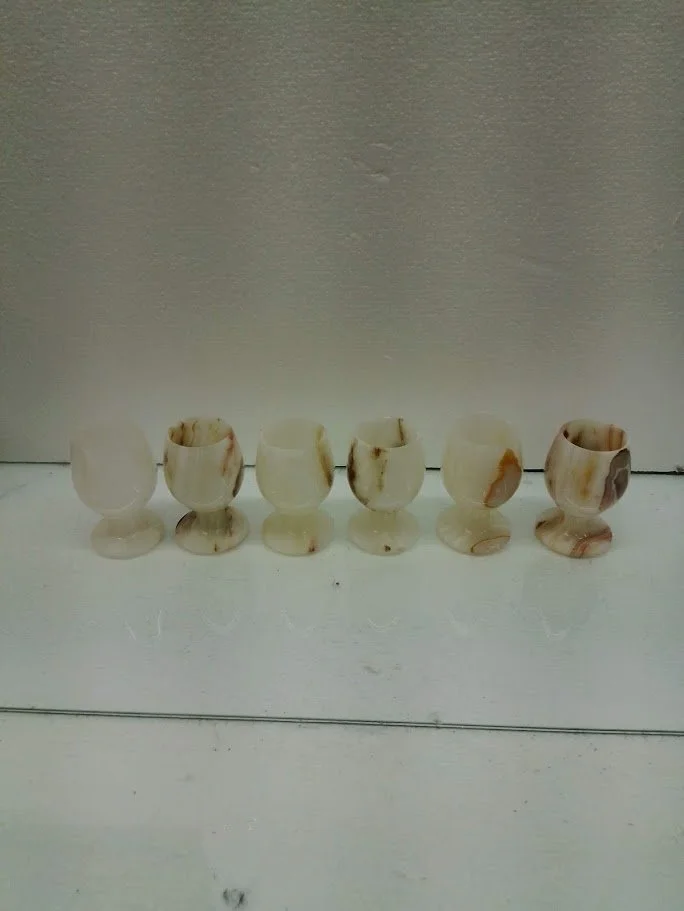 Six small, marble-like objects with various brown and beige patterns, placed in a row on a white surface against a gray background.