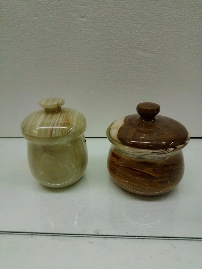 Two marble jars with lids on a white surface against a gray wall.