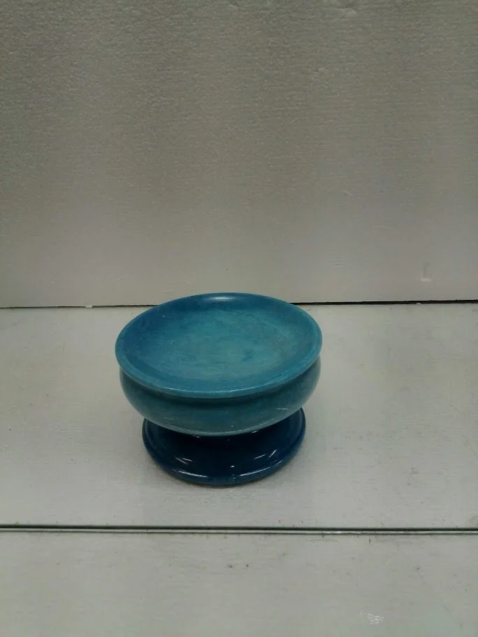 A small blue ceramic bowl with a glossy finish, placed on a matching dark blue saucer, all set against a plain light-colored background.