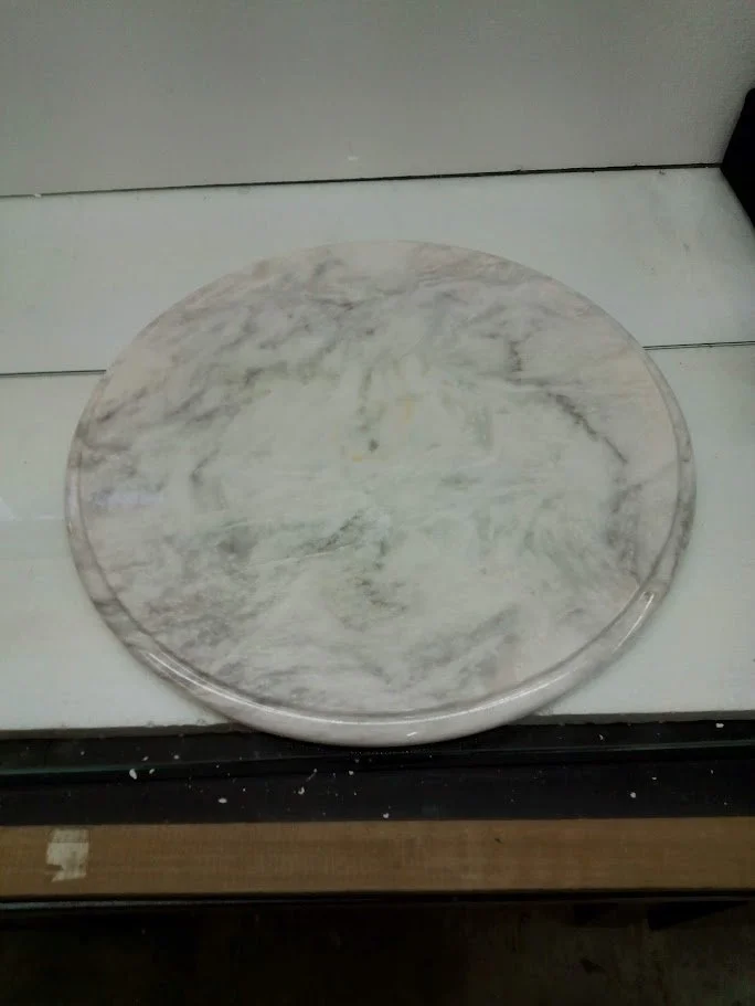 A round marble serving tray with a white and gray veined pattern placed on a white surface.