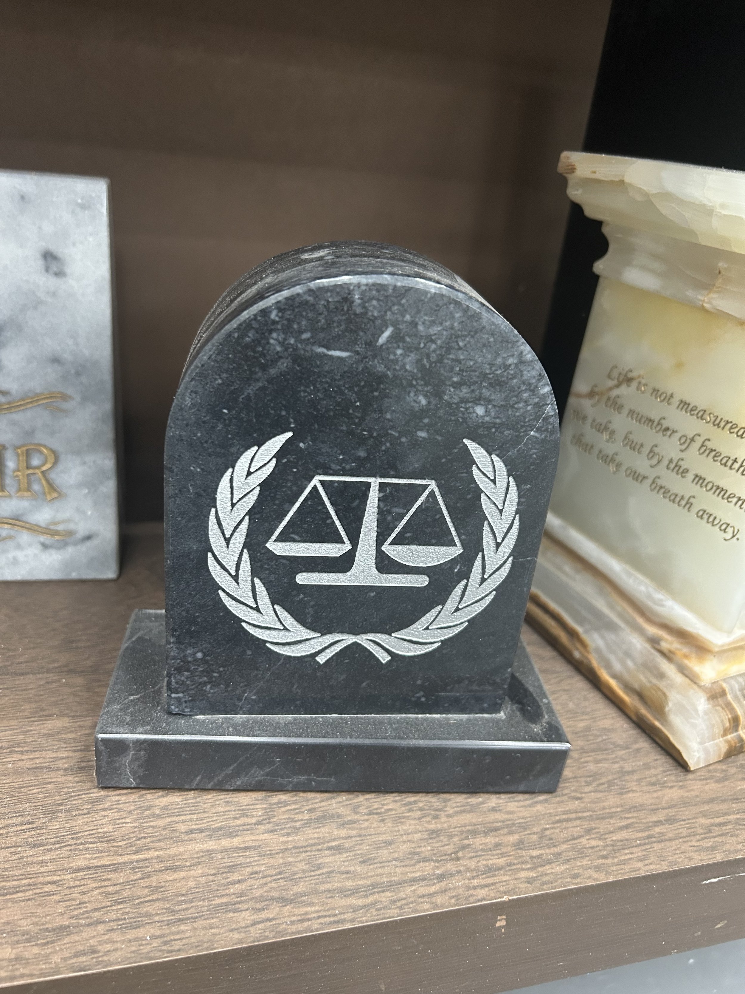 Black marble paperweight with white engraved scales of justice symbol, surrounded by a laurel wreath.