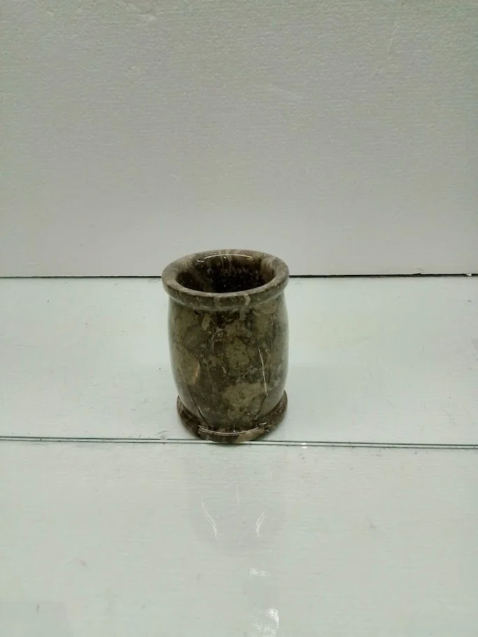 A small, round, brown marble mug with a smooth surface, sitting on a white wooden surface in front of a white wall.