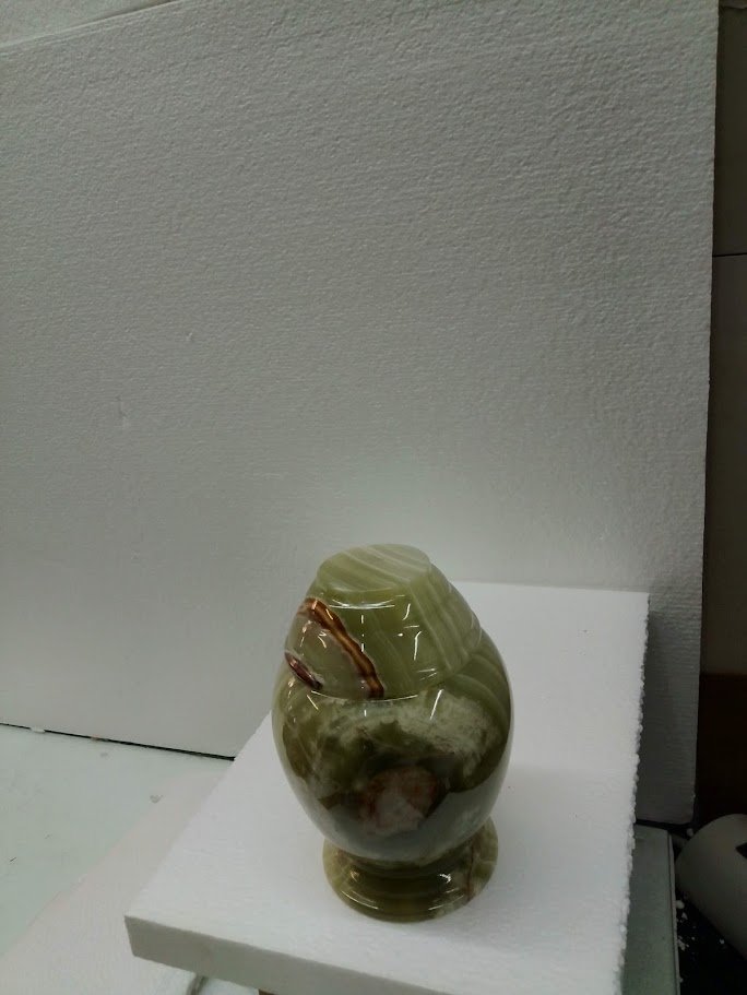 A decorative marble vase with a green and white pattern and a small metallic or copper-colored accent on a white surface.