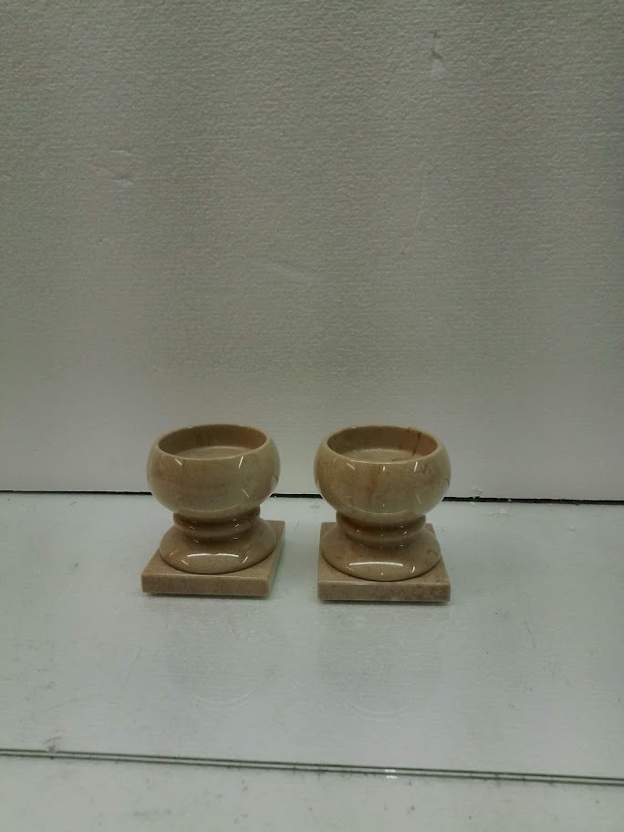 Two beige ceramic planters on square bases placed on a white surface against a light wall.