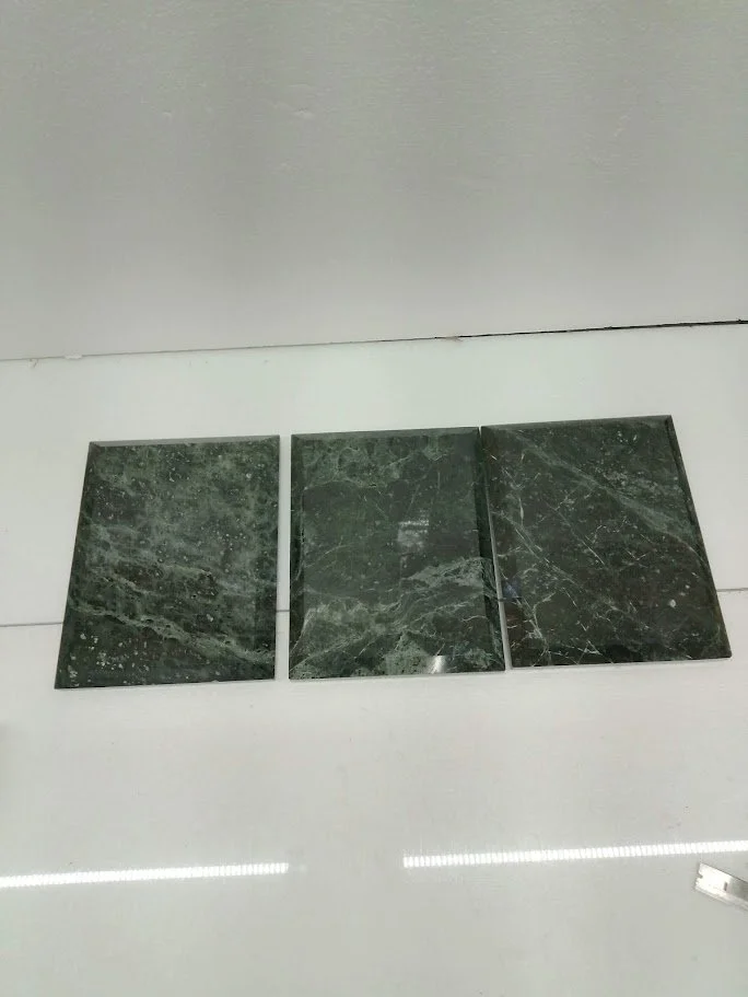 Three green marble tiles placed on a white floor with a gray wall behind them.