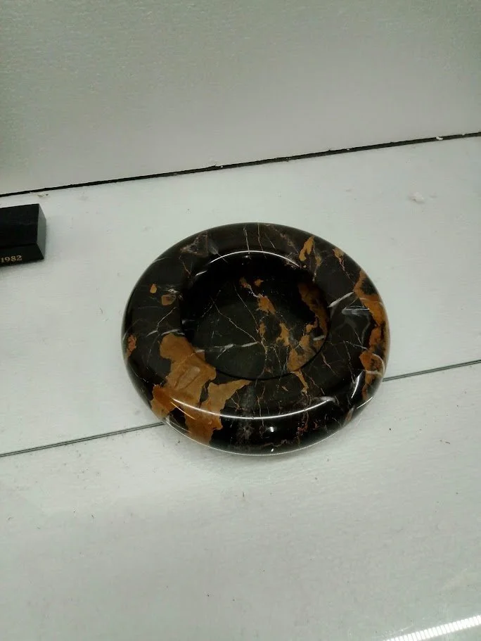 A round black marble ashtray with brown and white marble streaks on a white surface.