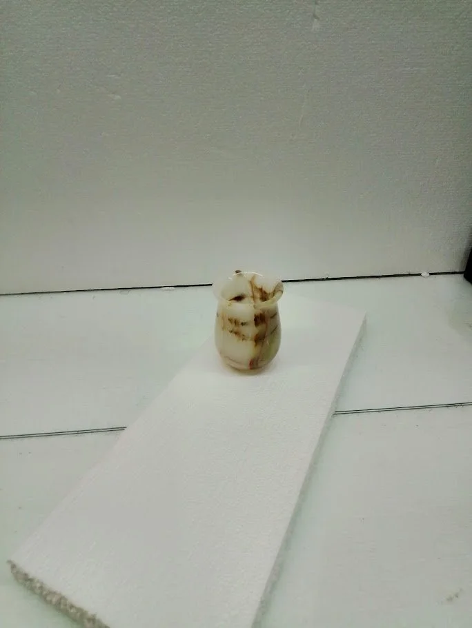 Small ceramic vase with brown and beige swirl pattern placed on a white rectangular platform against a light-colored wall.
