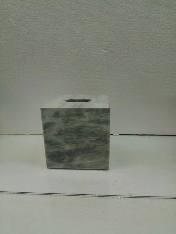 A marble tissue box holder on a white surface against a beige wall.